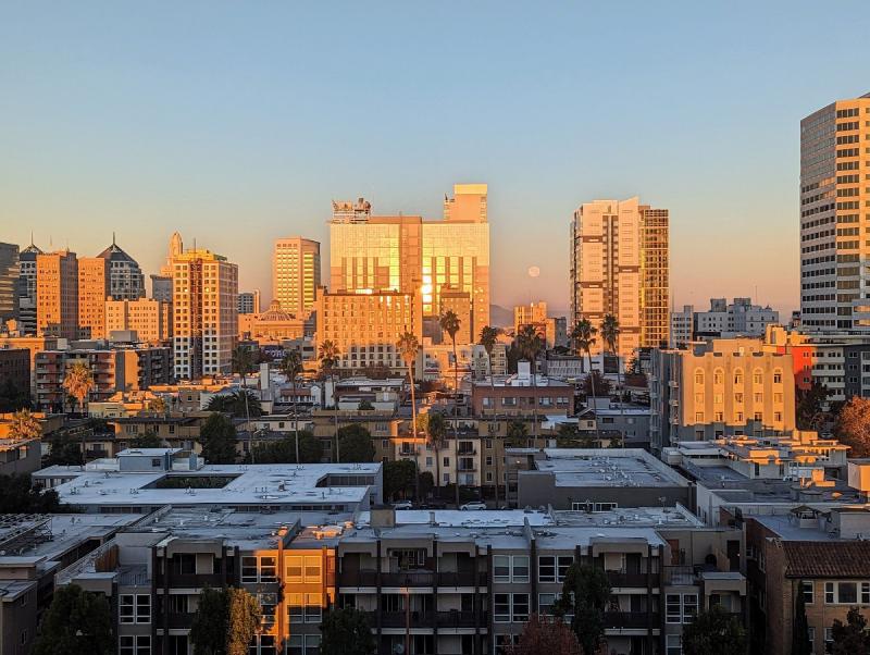 Sun reflecting off building looking west in Downtown oakland, with moon near horizon